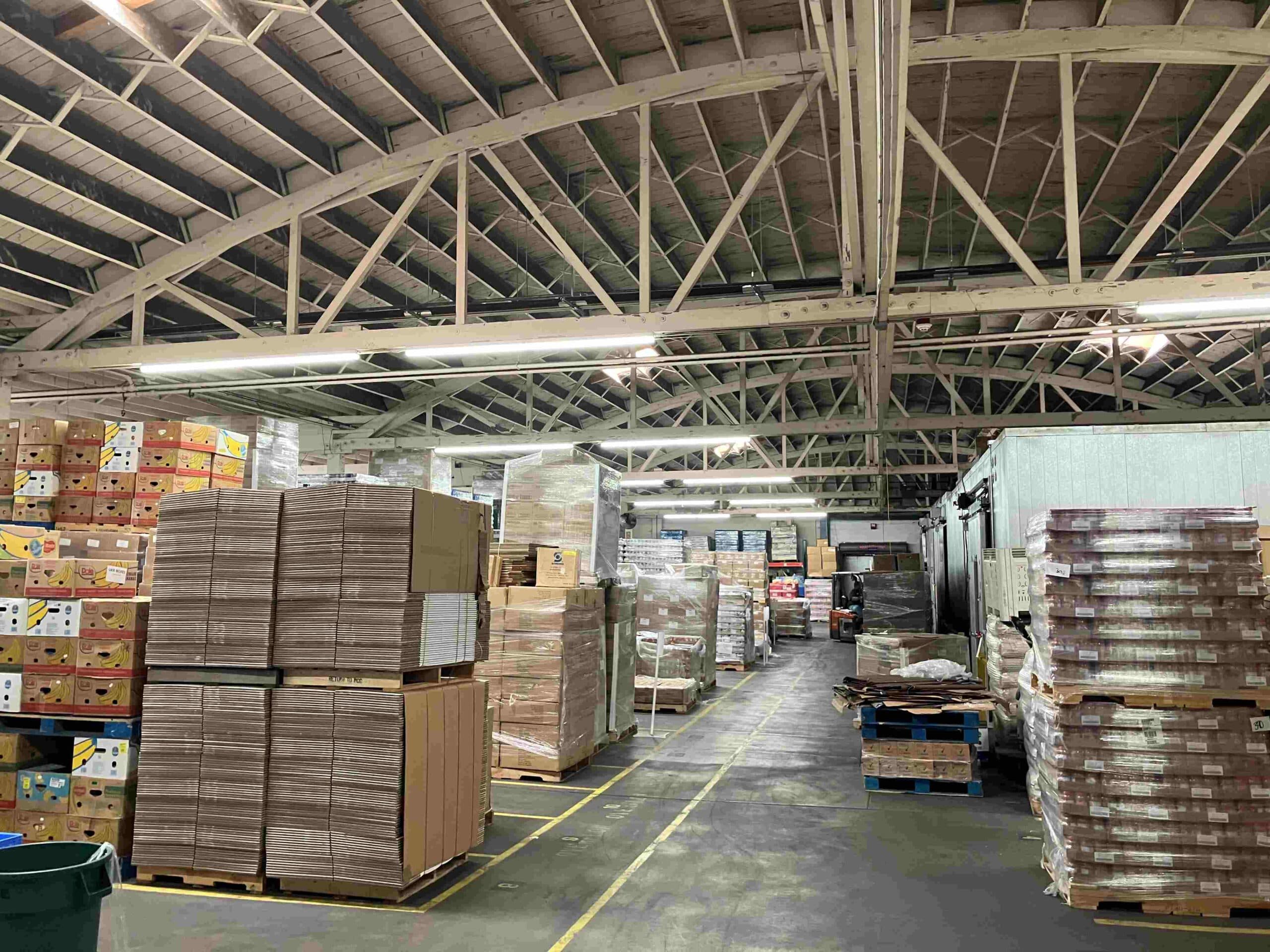 Linear LED fixtures suspended from bowstring trusses over pallet racking in a food distribution warehouse